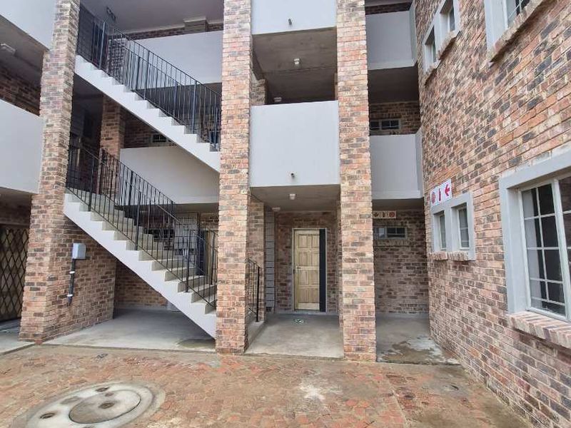 Exterior view of a multi-story apartment building featuring face brick construction, an open concrete staircase with iron railings, and a paved courtyard area.