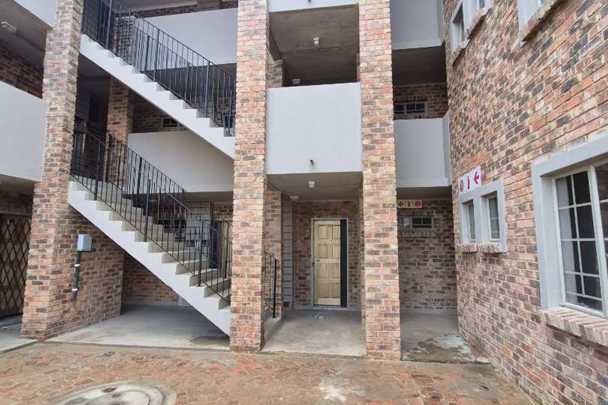 Exterior view of a multi-story apartment building featuring face brick construction, an open concrete staircase with iron railings, and a paved courtyard area.
