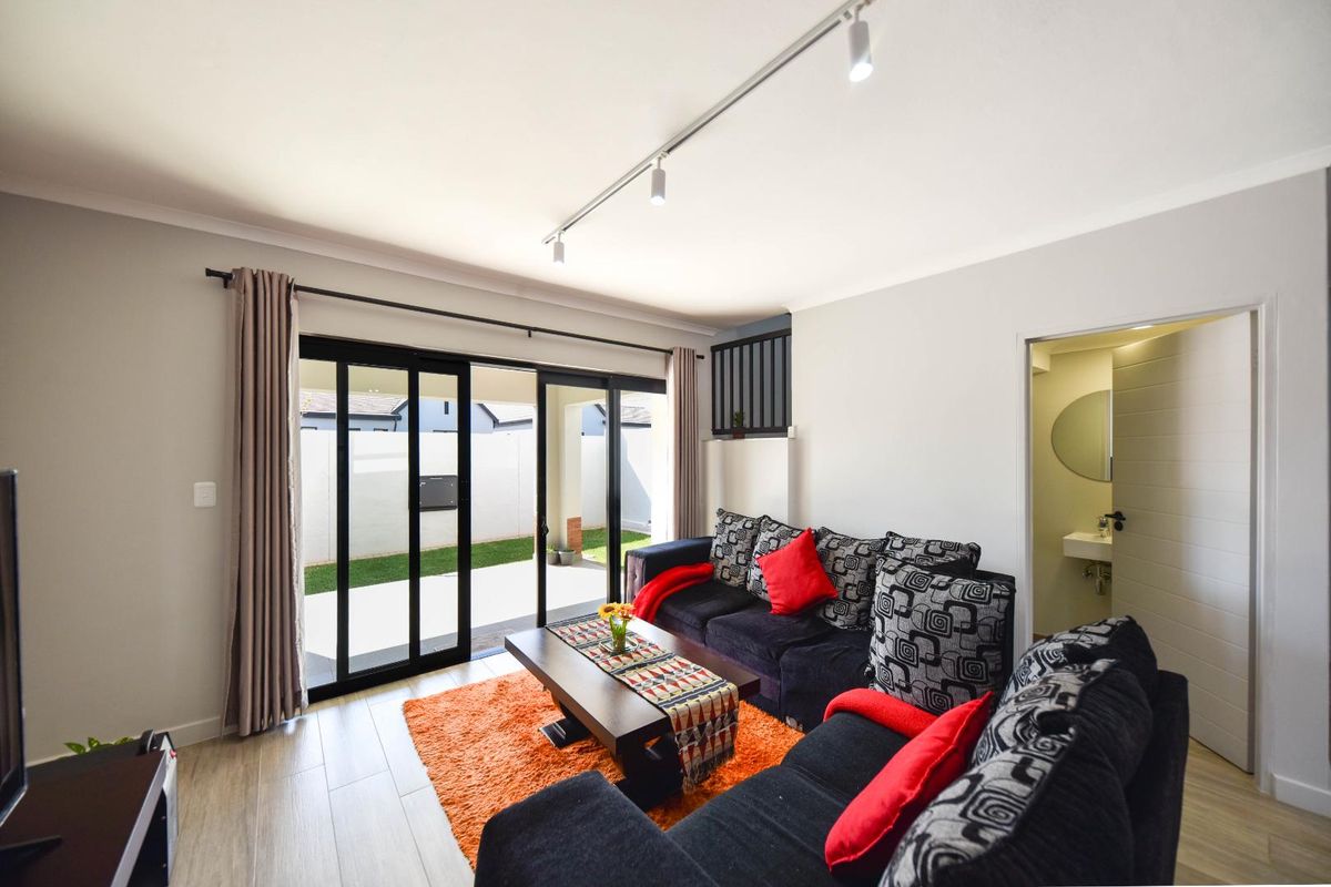 Bright living room featuring modern track lighting, laminate flooring, and large sliding glass doors providing direct access to the rear patio and garden area.