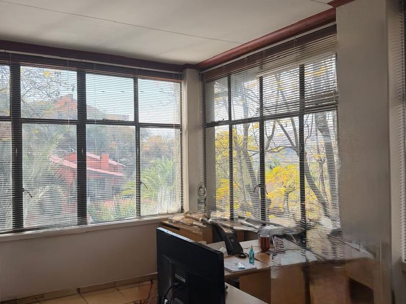 A functional office space featuring large windows with venetian blinds, tiled flooring, and overhead fluorescent lighting, providing ample natural light.