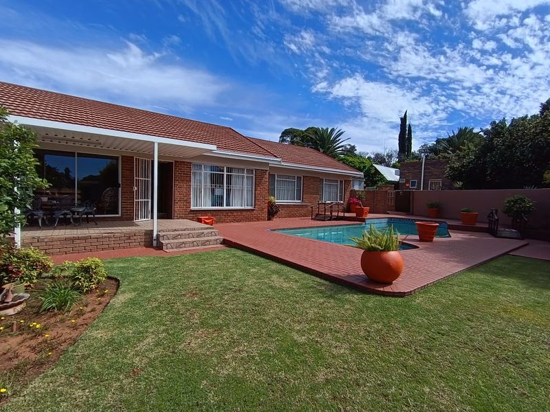 Rear exterior view featuring a brick-paved patio, a swimming pool, and a well-maintained lawn, providing an ideal space for outdoor entertainment.