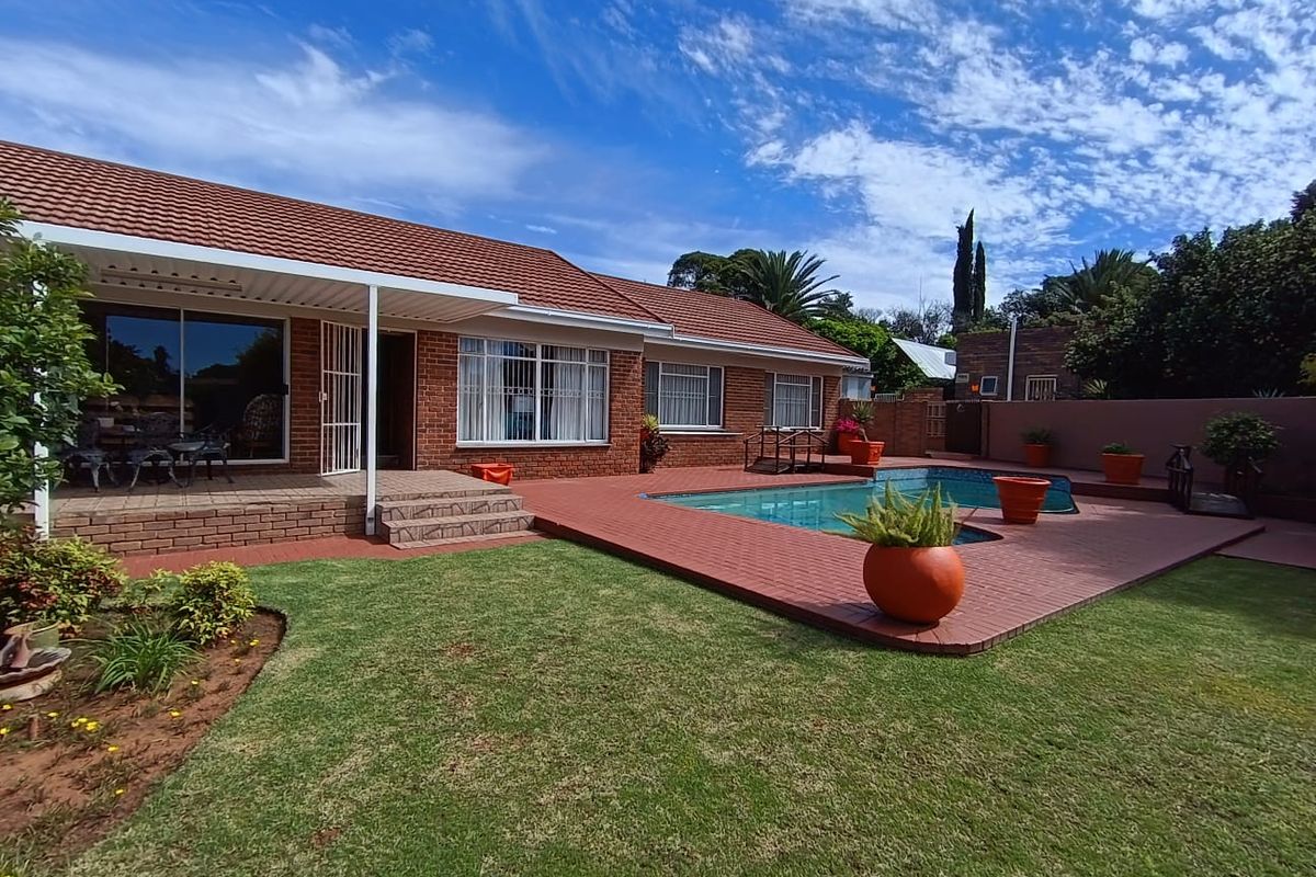 Rear exterior view featuring a brick-paved patio, a swimming pool, and a well-maintained lawn, providing an ideal space for outdoor entertainment.