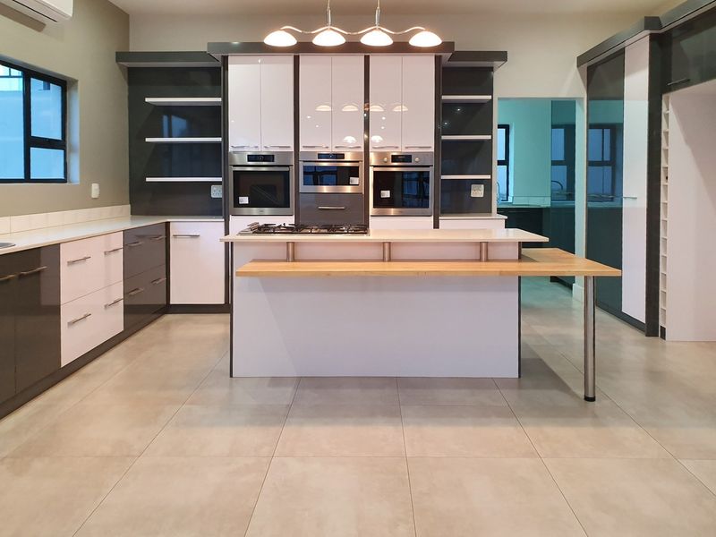 Modern kitchen featuring high-gloss cabinetry, built-in appliances, a central island with a breakfast bar, and neutral tiled flooring.