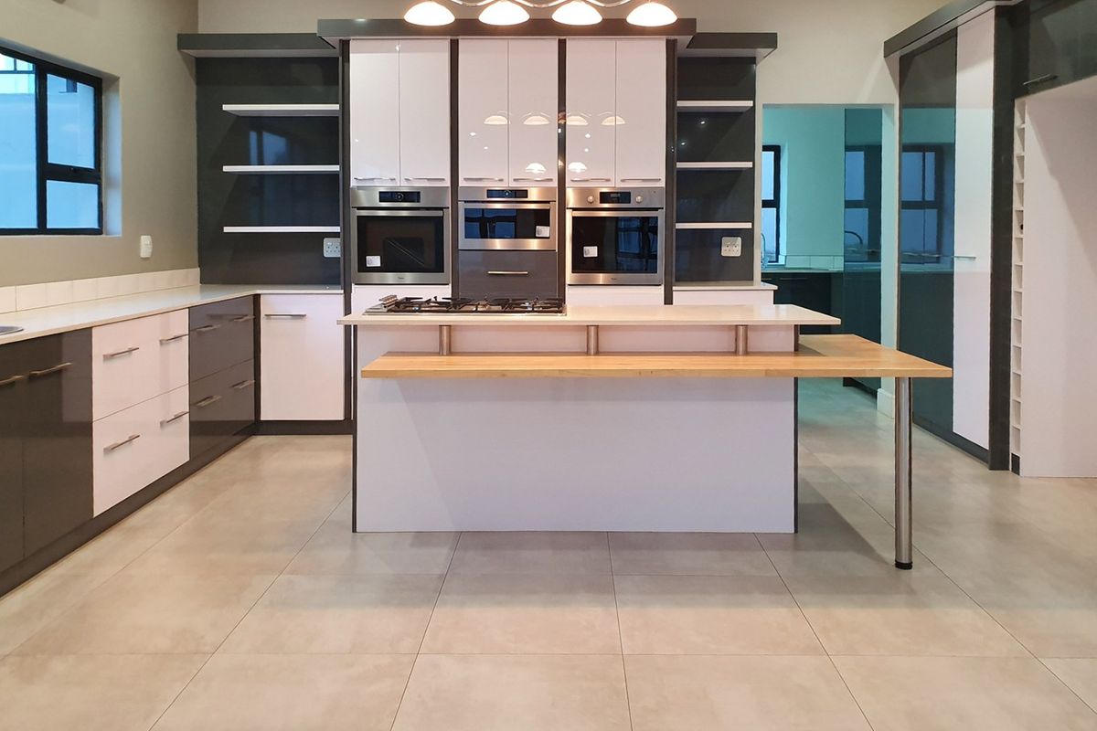 Modern kitchen featuring high-gloss cabinetry, built-in appliances, a central island with a breakfast bar, and neutral tiled flooring.