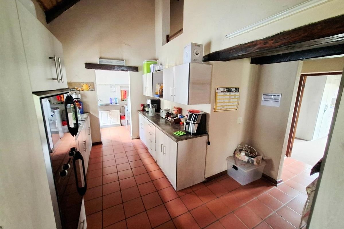 A kitchen featuring vaulted ceilings with exposed timber beams, tiled flooring, and built-in cabinetry with laminate countertops.