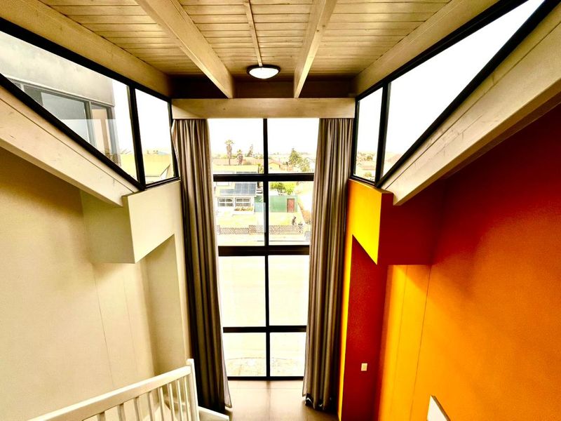 A bright, double-volume hallway featuring a vaulted timber ceiling, expansive windows providing natural light, and a modern staircase railing.