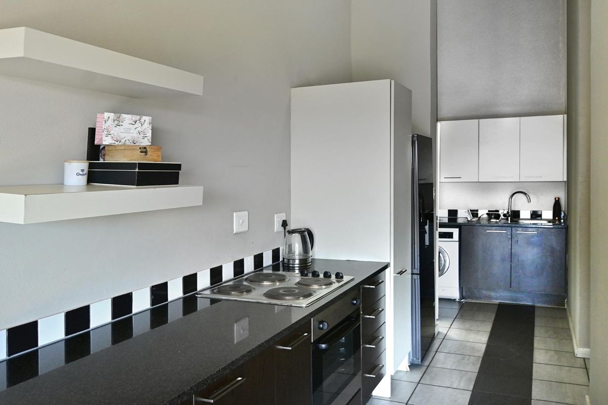 A functional kitchen featuring dark cabinetry, granite countertops, a built-in oven and hob, and a tiled backsplash, with an adjacent laundry area.