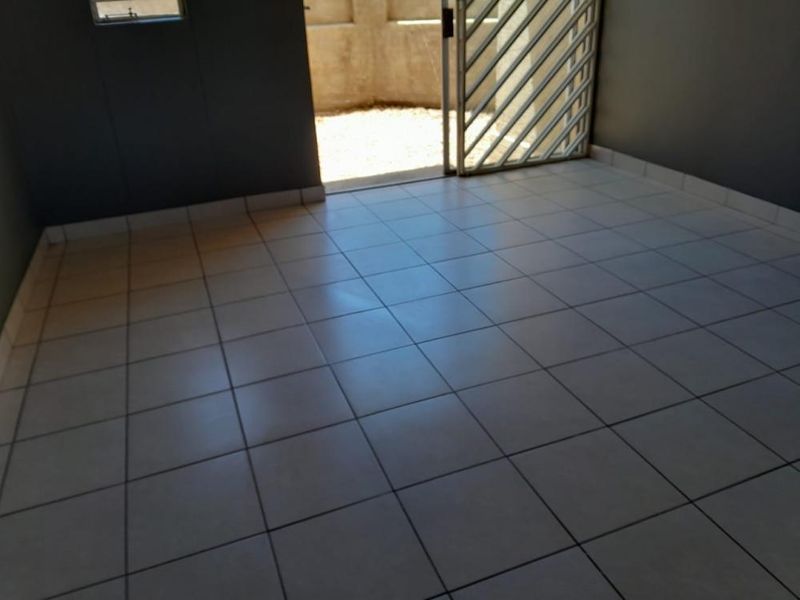 An empty living area featuring neutral tiled flooring and a security gate leading to an outdoor space.