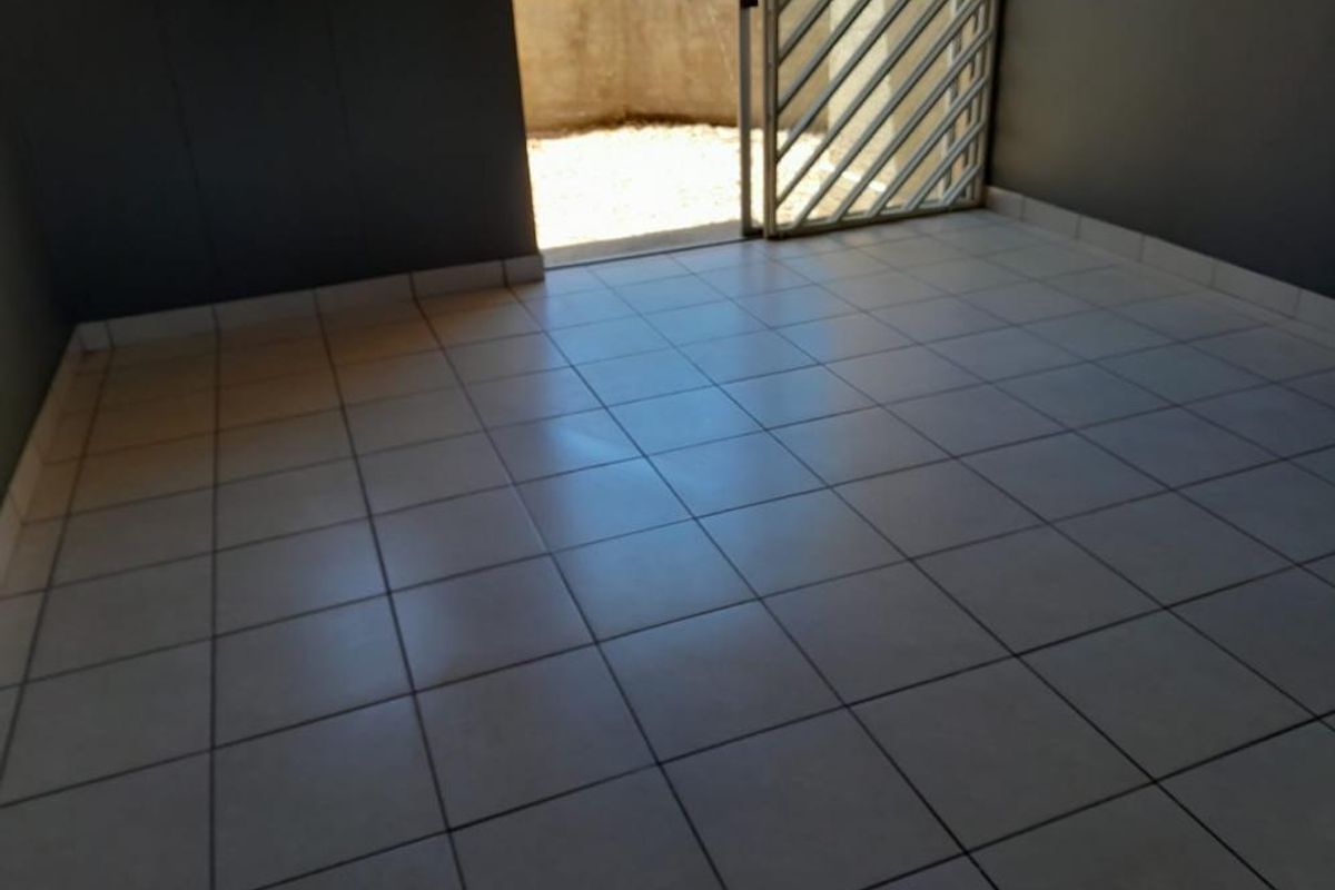 An empty living area featuring neutral tiled flooring and a security gate leading to an outdoor space.