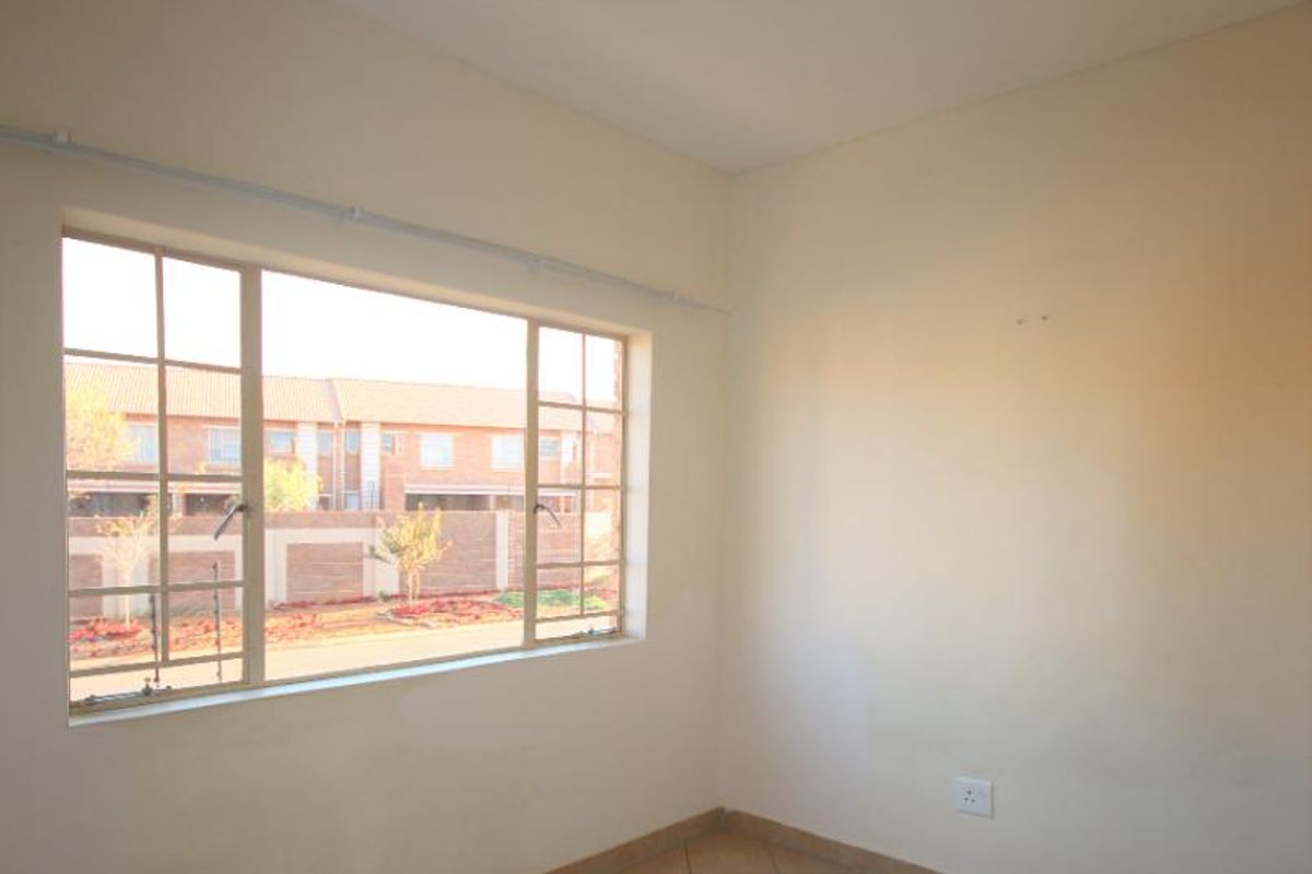 A bright, empty bedroom featuring tiled flooring, a large window with a curtain rail, and a central ceiling light fixture.