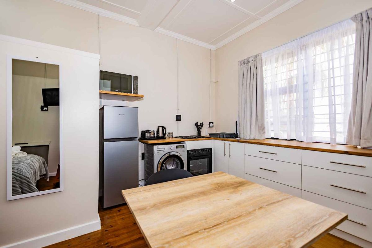 Compact kitchen area featuring white cabinetry, wooden countertops, built-in oven, and integrated laundry facilities, finished with timber flooring and crown molding.