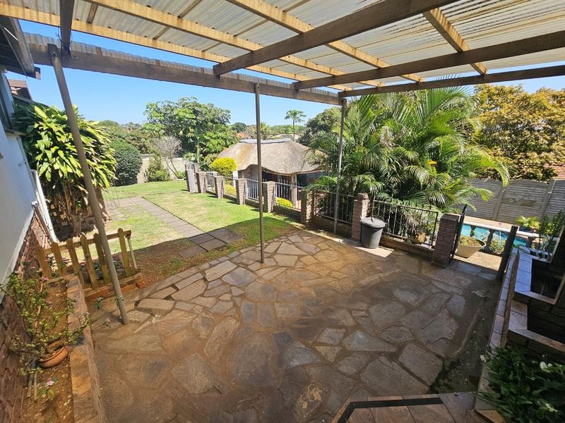 A covered outdoor patio area featuring flagstone paving and a timber pergola, overlooking a private garden and swimming pool.