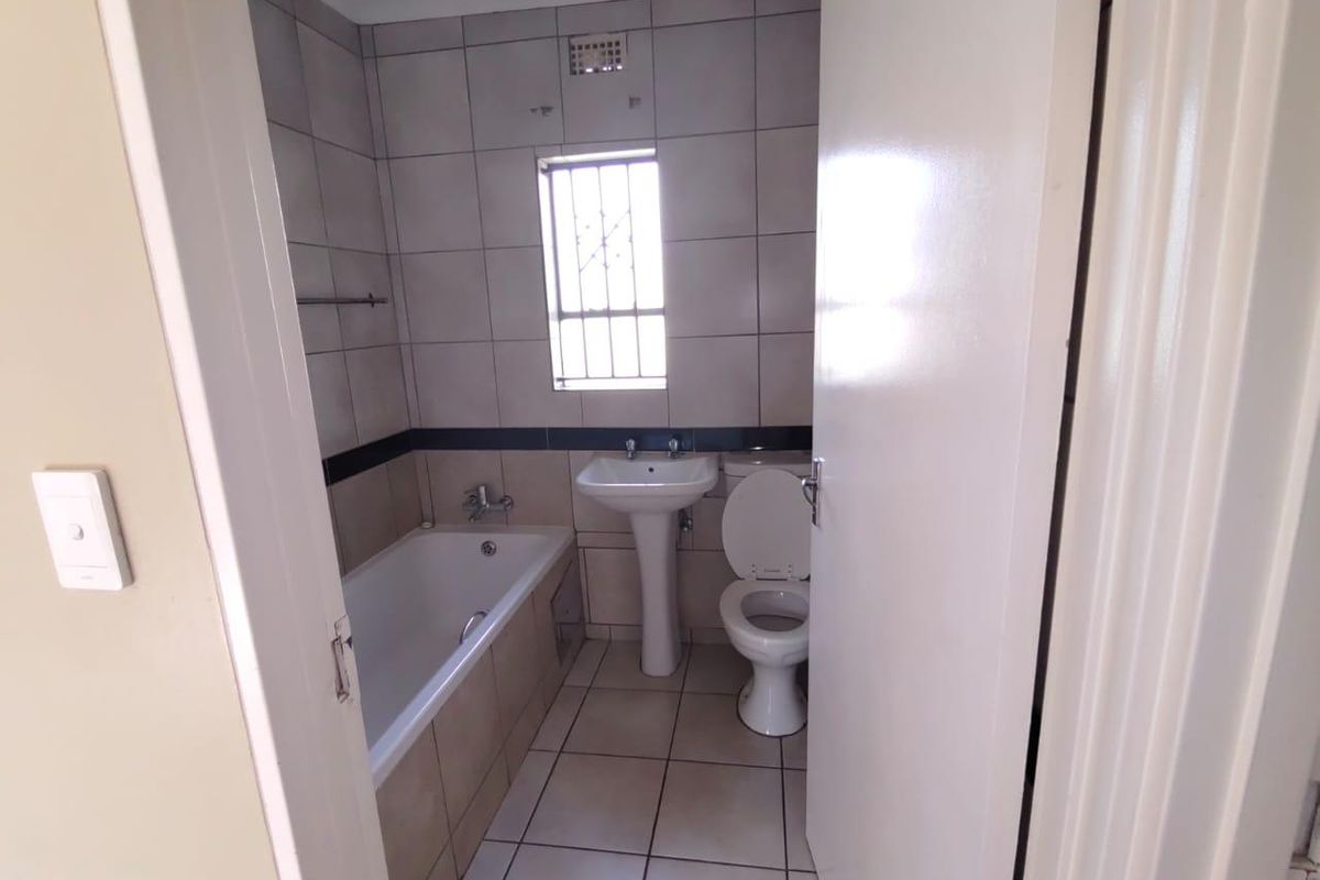 A functional bathroom featuring a bathtub, pedestal sink, and toilet with neutral wall and floor tiling.