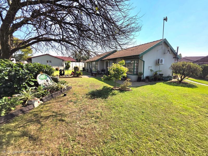 Rear view of the house featuring a tiled roof, concrete patio area, and a spacious garden with established trees.