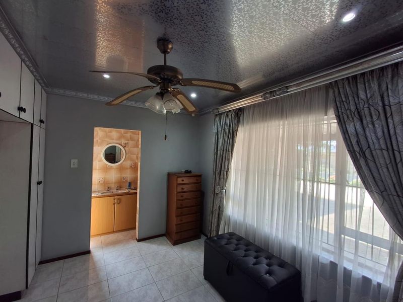 A bedroom featuring tiled flooring, built-in cupboards, a ceiling fan, and an adjoining en-suite vanity area with a mirror.