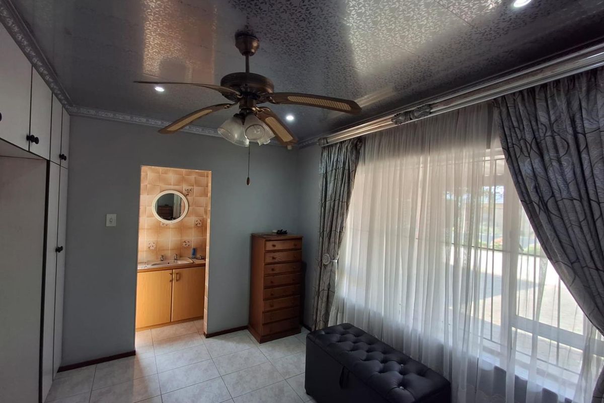 A bedroom featuring tiled flooring, built-in cupboards, a ceiling fan, and an adjoining en-suite vanity area with a mirror.