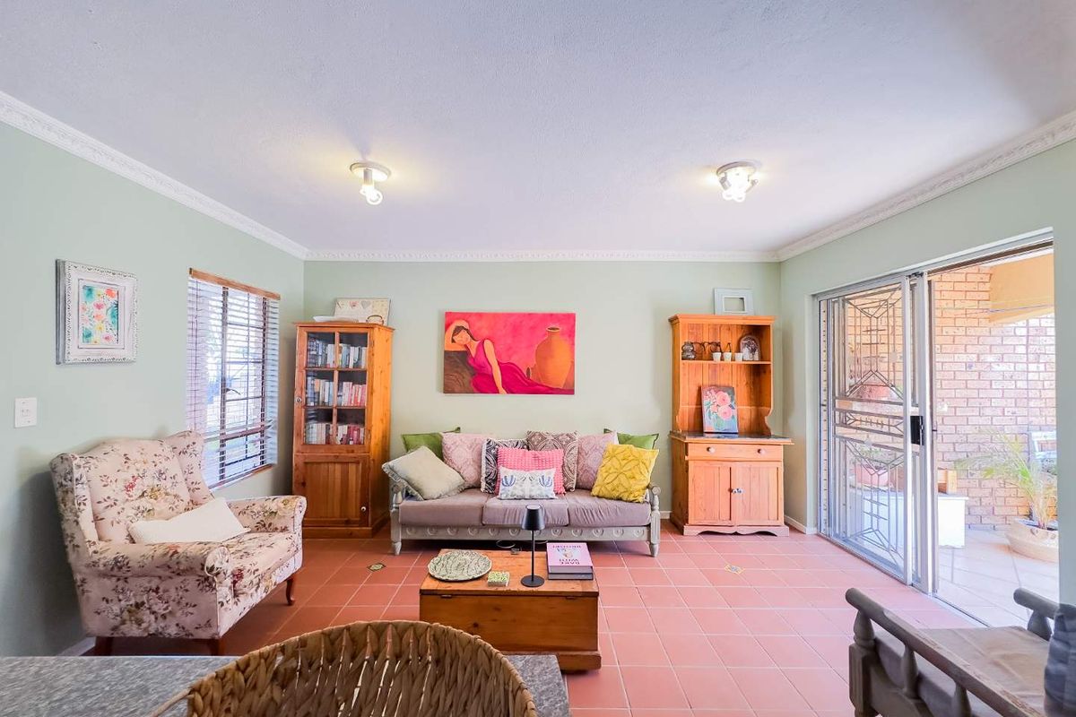 A living room featuring terracotta floor tiles, crown molding, and a sliding glass door with a security gate leading to an outdoor patio area.