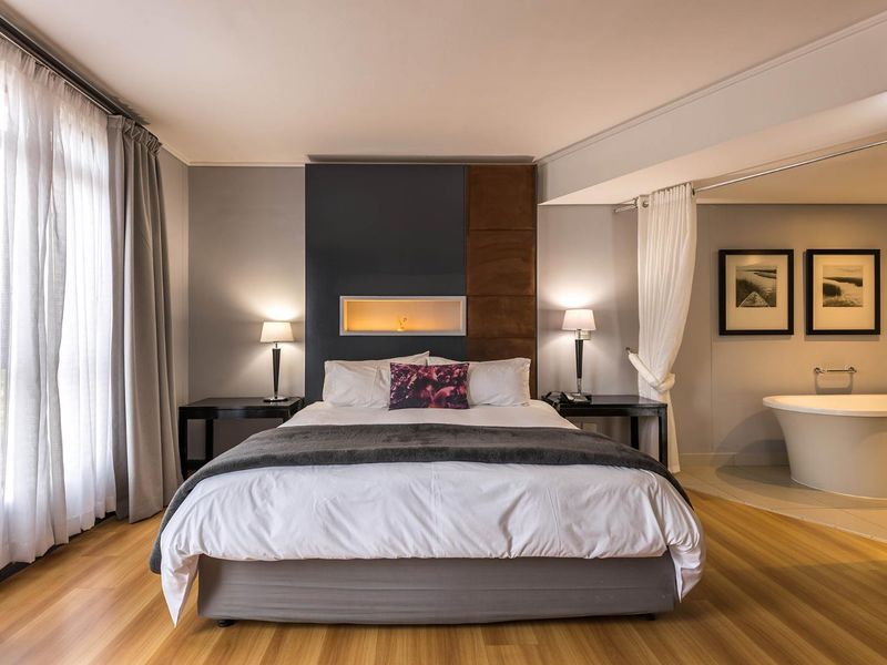 Spacious bedroom featuring modern laminate flooring, a decorative recessed wall niche, and an integrated open-plan ensuite area with a freestanding bathtub.