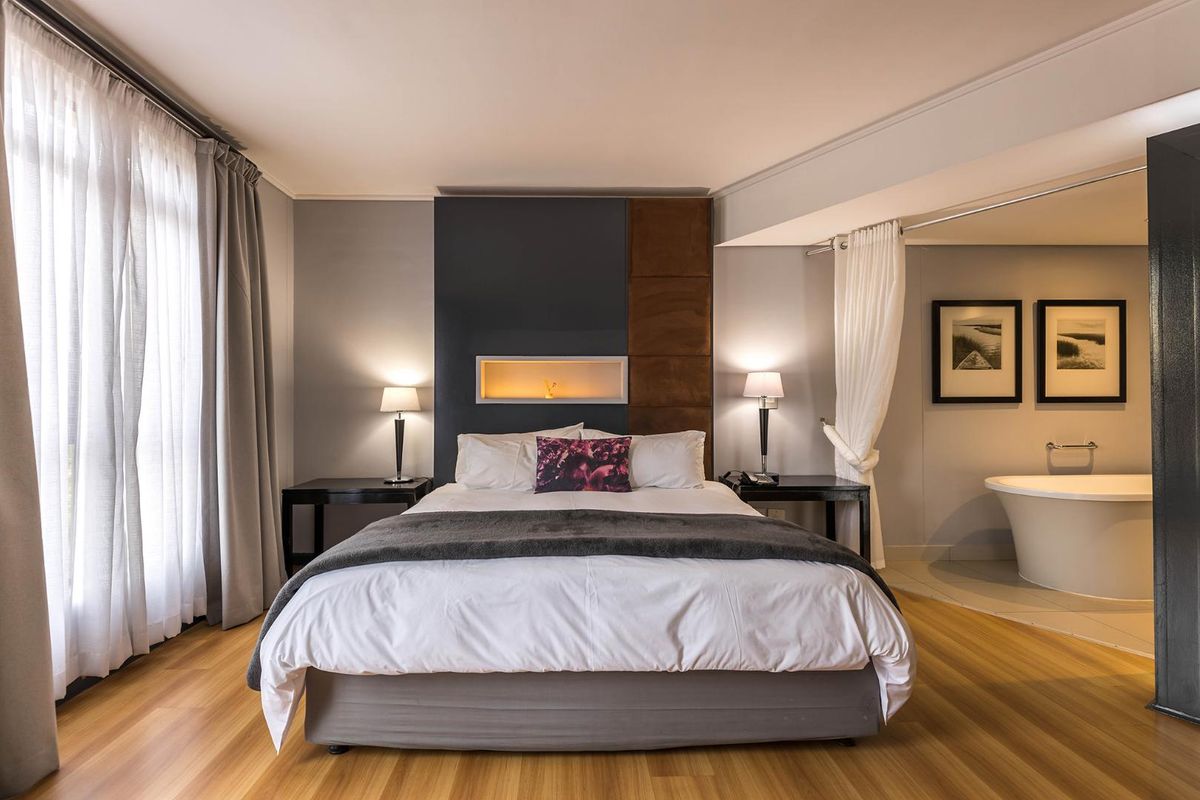 Spacious bedroom featuring modern laminate flooring, a decorative recessed wall niche, and an integrated open-plan ensuite area with a freestanding bathtub.