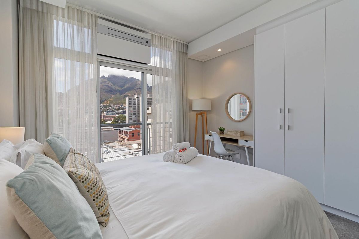 Modern bedroom featuring a built-in wardrobe, wall-mounted air conditioning, and a sliding glass door leading to a balcony with mountain and city views.