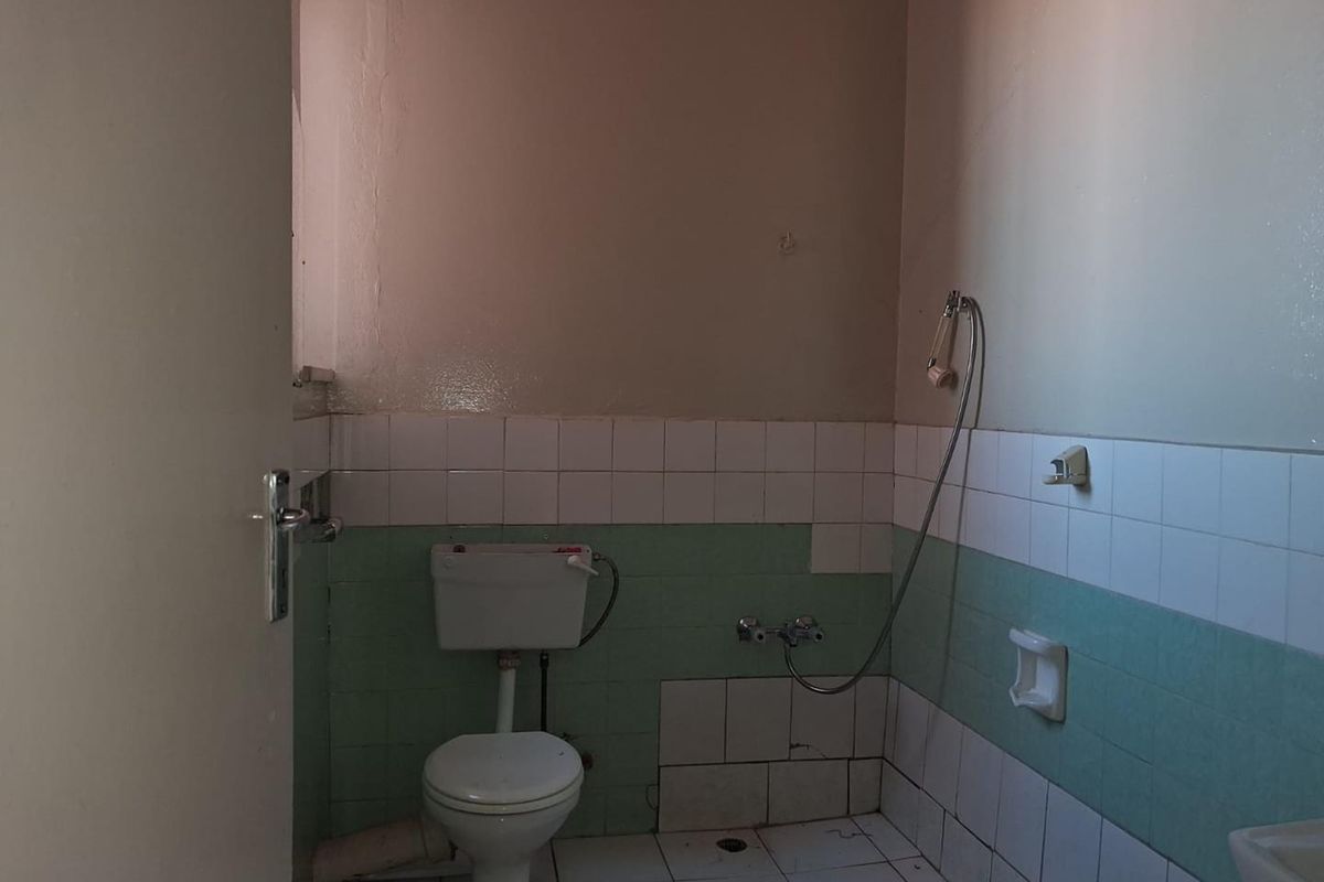 A dated bathroom featuring a toilet, handheld shower fixture, and partially tiled walls in need of renovation and repair.