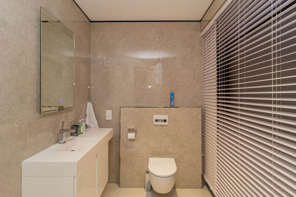 Modern bathroom featuring floor-to-ceiling neutral tiling, a wall-mounted vanity with integrated basin, and a concealed cistern toilet.