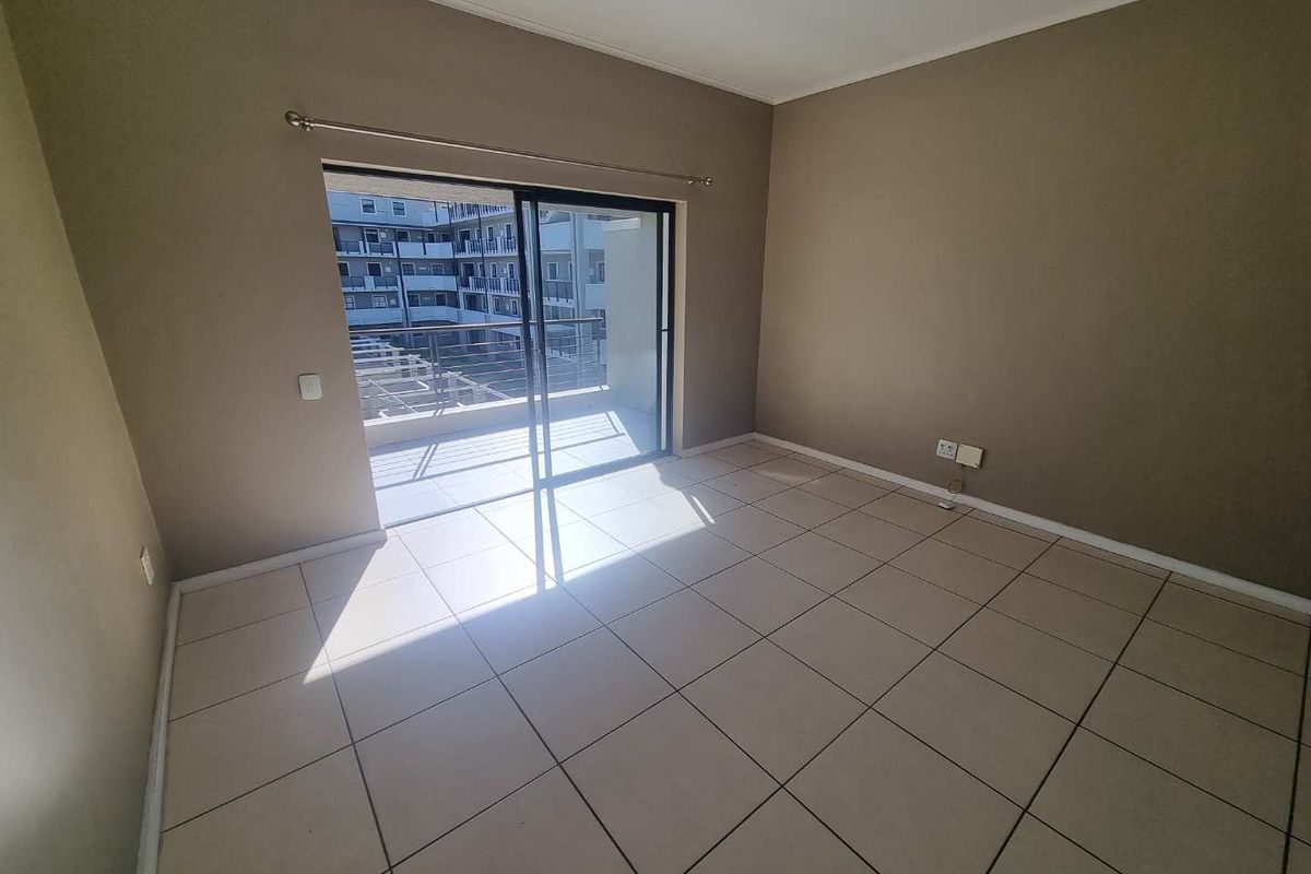 An empty living room featuring neutral tiled flooring and a sliding glass door providing access to an outdoor balcony area.