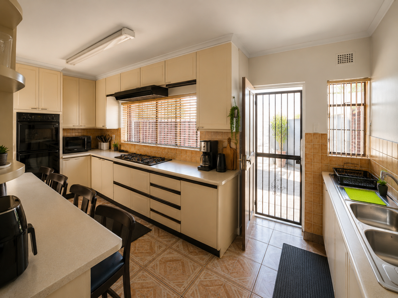A functional kitchen featuring cream cabinetry, built-in oven, gas cooktop, and a double bowl sink, with direct access to an outdoor area via a security gate.