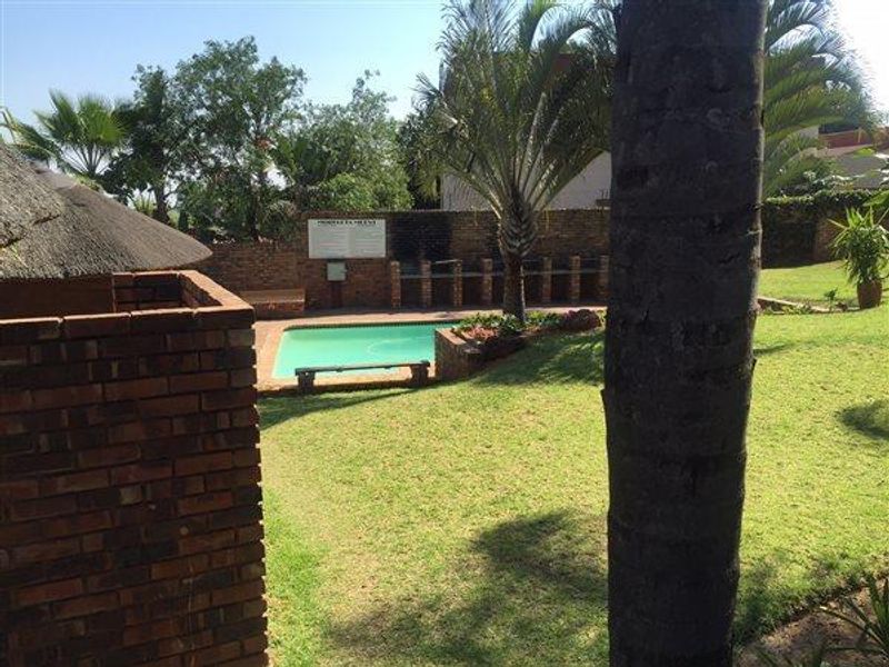 Outdoor communal pool area featuring a swimming pool, brick boundary wall, and built-in braai facilities set within a landscaped garden.