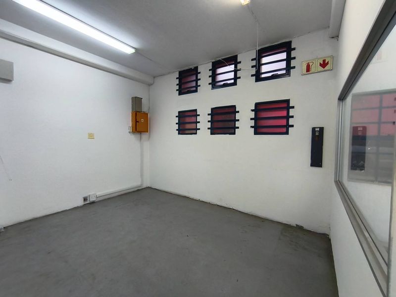 A functional industrial utility space featuring concrete flooring, secure louvre windows, and wall-mounted electrical infrastructure, suitable for storage or workshop use.