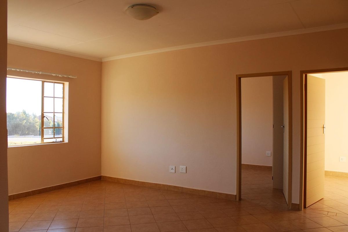 A bright, empty bedroom featuring tiled flooring, neutral wall finishes, and access to an adjoining room through a doorway.