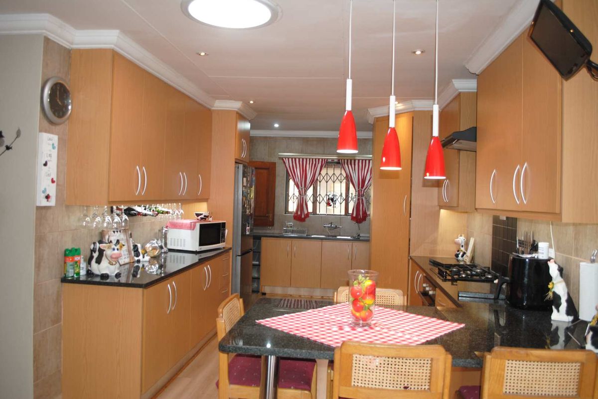 A functional kitchen featuring light wood cabinetry, dark granite countertops, a built-in gas hob, and an integrated dining area with pendant lighting.