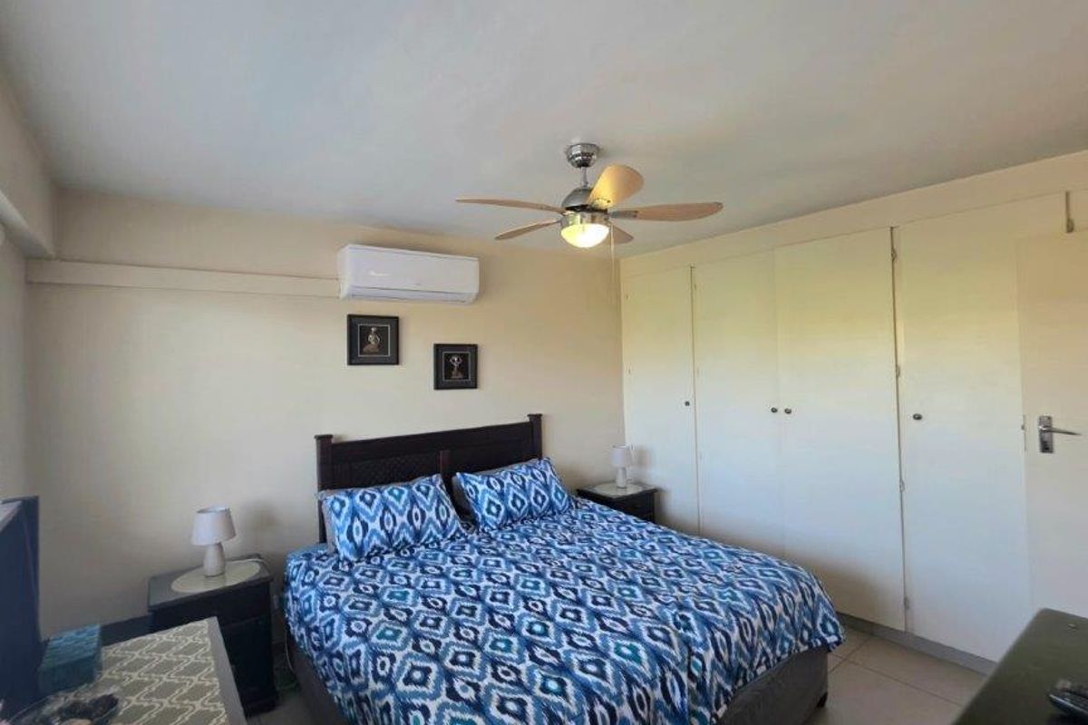 A functional bedroom featuring built-in cupboards, a ceiling fan, and a wall-mounted air conditioning unit.