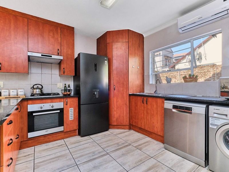 Functional kitchen featuring wood-finish cabinetry, granite countertops, built-in oven, gas hob, and integrated space for appliances with tiled flooring and backsplash.