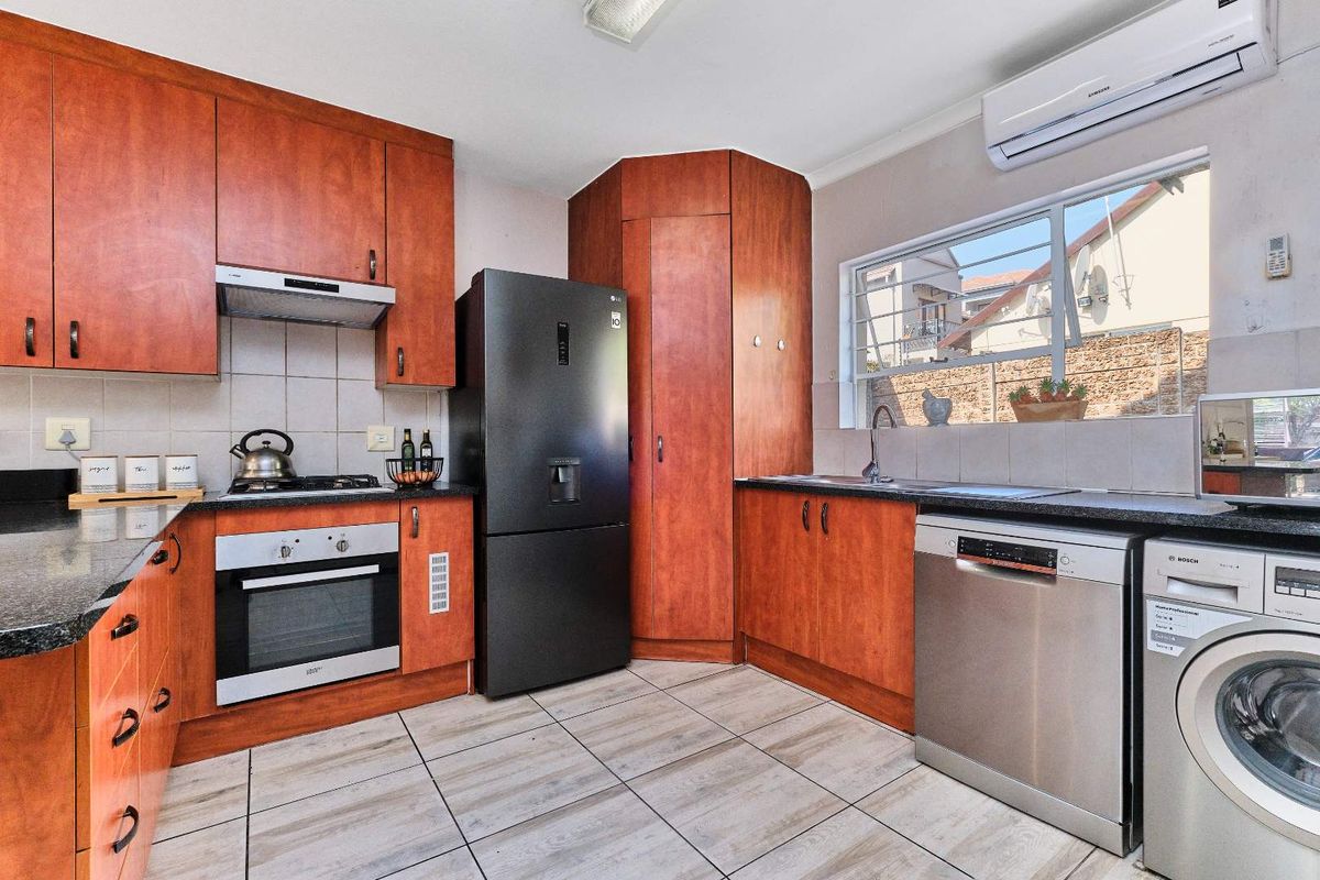Functional kitchen featuring wood-finish cabinetry, granite countertops, built-in oven, gas hob, and integrated space for appliances with tiled flooring and backsplash.