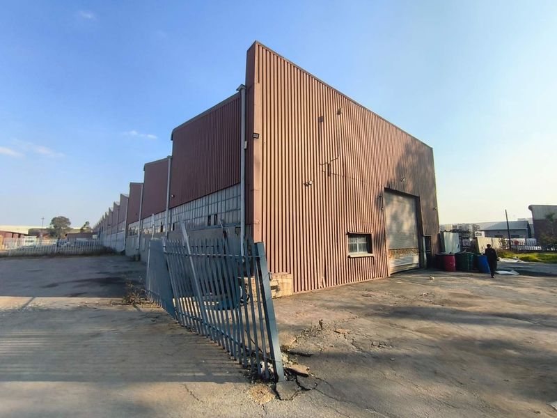 Exterior view of an industrial warehouse featuring corrugated metal cladding, a large roller shutter door, and surrounding concrete yard space with perimeter fencing.