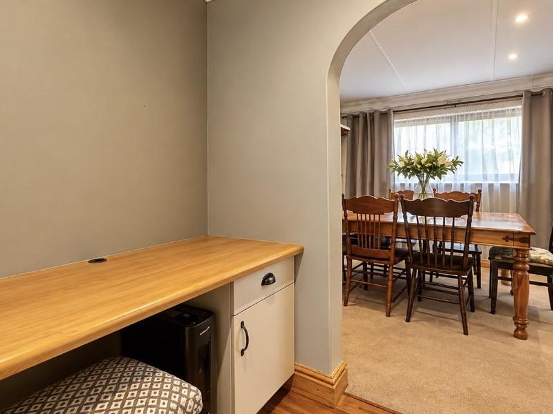A functional home office nook featuring a built-in desk and cabinetry, seamlessly connected to the dining area through a classic arched doorway.