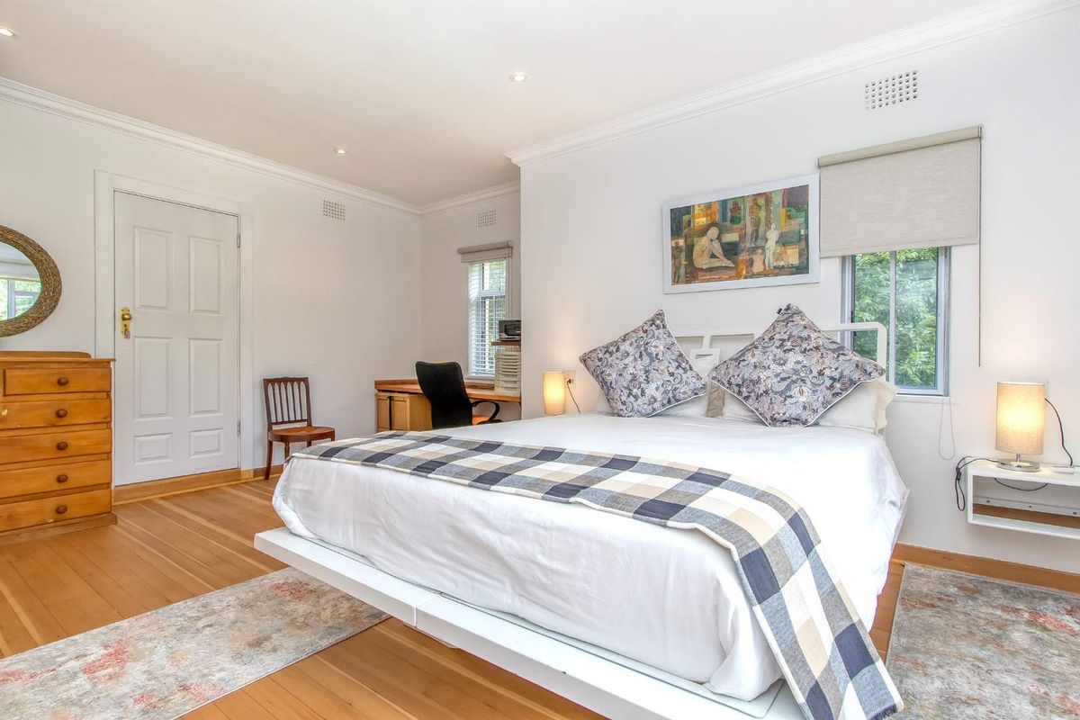 A bright and well-maintained bedroom featuring polished timber flooring, crown molding, and a built-in workspace area.
