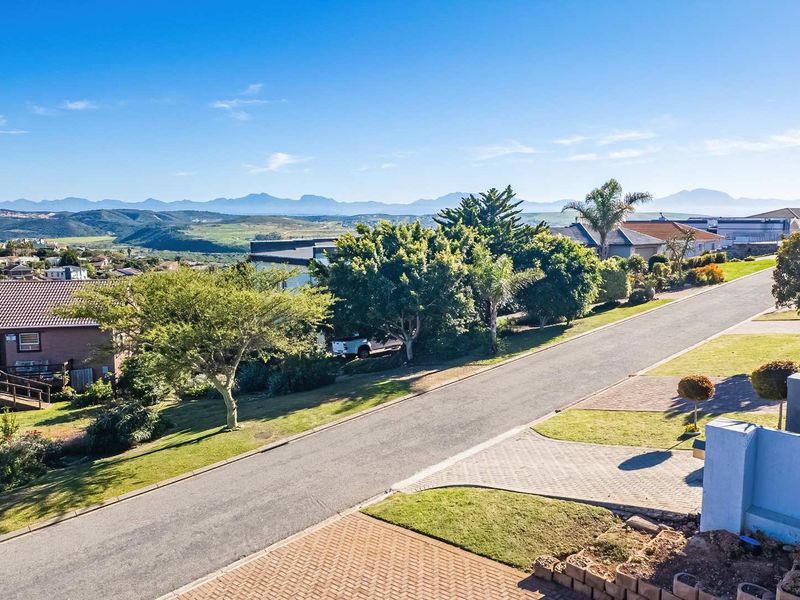 Elevated view overlooking the residential street, surrounding neighborhood, and distant mountain range under a clear blue sky.