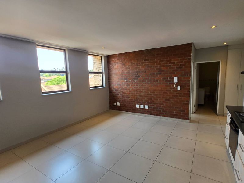 Spacious open-plan living area featuring a striking exposed brick wall, modern tiled flooring, and a sleek kitchen with granite countertops and built-in appliances.
