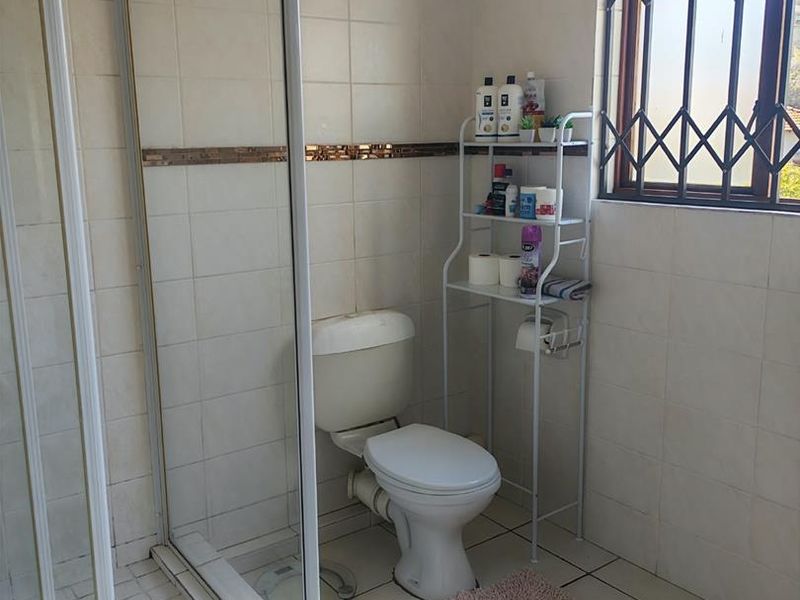 A functional bathroom featuring a glass-enclosed shower, toilet, and neutral wall and floor tiling with a security-fitted window.