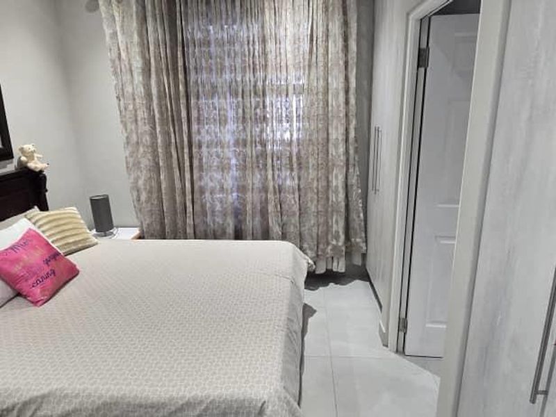 A well-maintained bedroom featuring built-in cupboards, tiled flooring, and a large wall-mounted mirror.