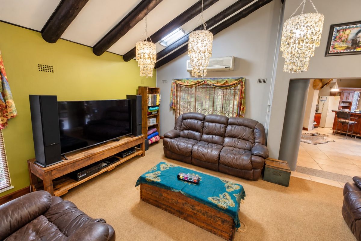 Spacious living room featuring high vaulted ceilings with exposed timber beams, a skylight, and wall-mounted air conditioning, with an open flow to the kitchen area.