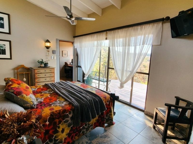 A well-lit bedroom featuring exposed beam ceilings, tiled flooring, and an exposed brick accent wall, with direct access to an outdoor deck area.