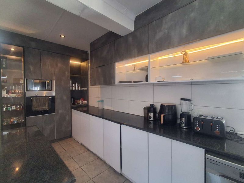 Modern kitchen featuring dark grey and white cabinetry, granite countertops, built-in oven and microwave, and integrated under-cabinet lighting.