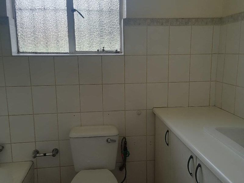 A dated bathroom featuring a toilet, vanity cabinet, and bathtub with tiled walls and flooring, offering potential for a modern renovation.