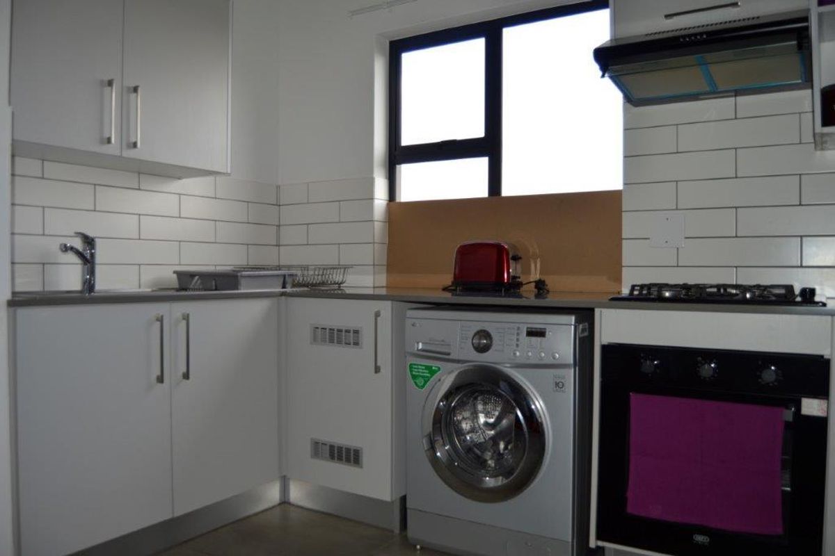 Modern kitchen featuring white cabinetry, subway tile backsplash, built-in oven, gas hob, extractor fan, and integrated laundry appliance space.