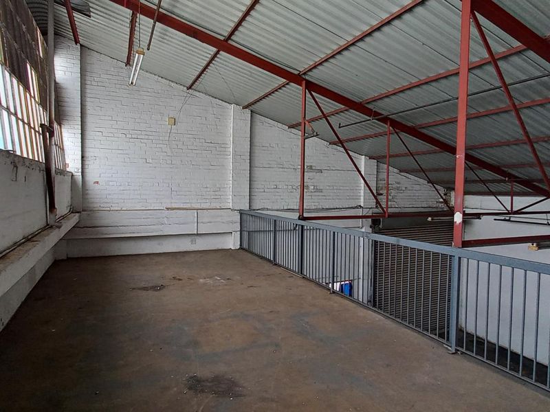 An industrial mezzanine level featuring exposed steel roof trusses, painted brick walls, and metal safety railings, suitable for storage or workshop conversion.