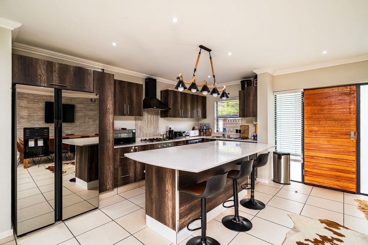 Modern kitchen featuring dark wood cabinetry, a large central island with quartz countertops, gas hob, extractor fan, and tiled flooring.