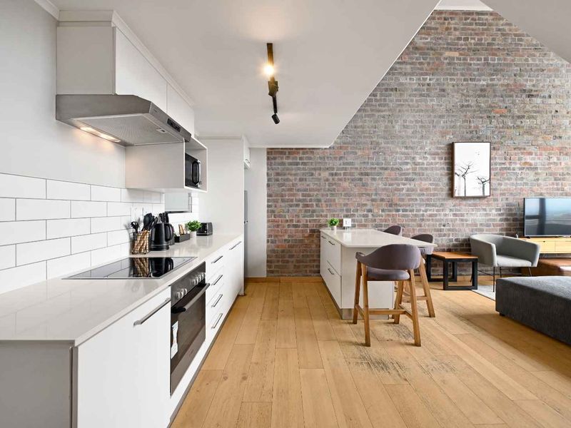 Modern open-plan living area featuring a sleek kitchen with built-in appliances, subway tile backsplash, and a striking exposed brick feature wall.